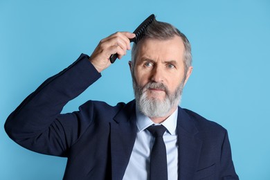 Photo of Handsome man combing his hair on light blue background