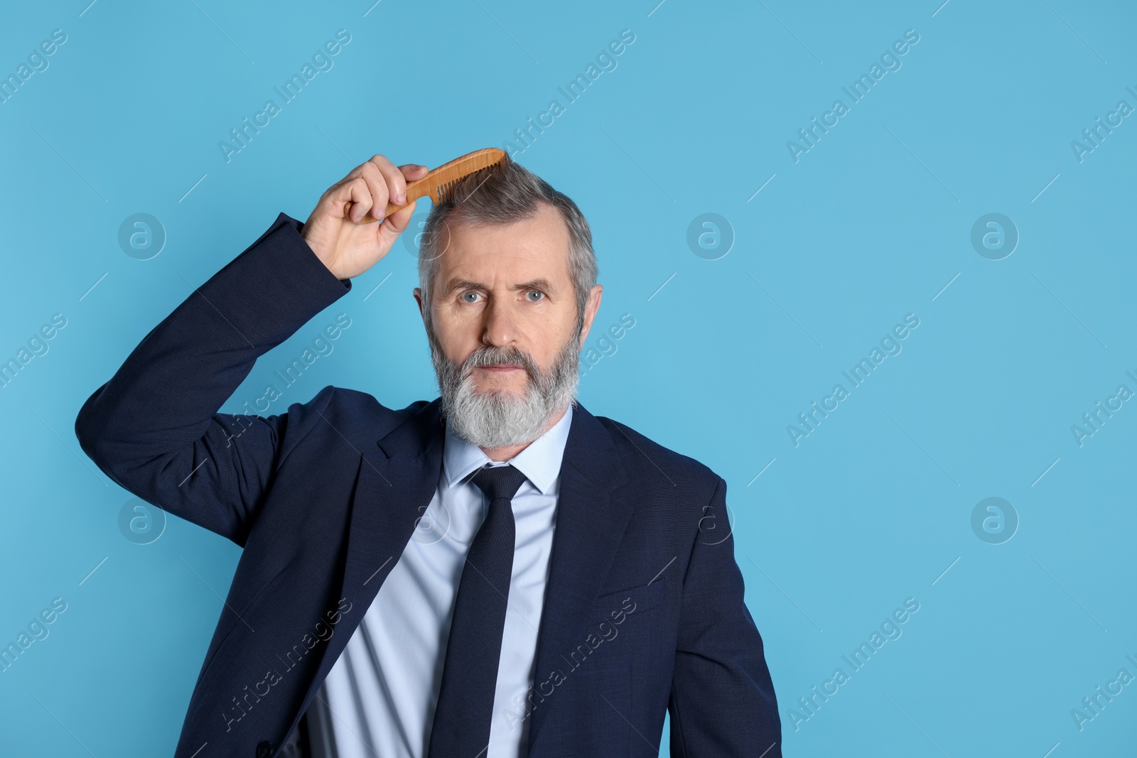 Photo of Handsome man combing his hair on light blue background. Space for text