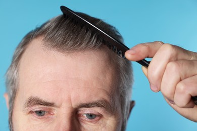 Photo of Man combing his hair on light blue background, closeup