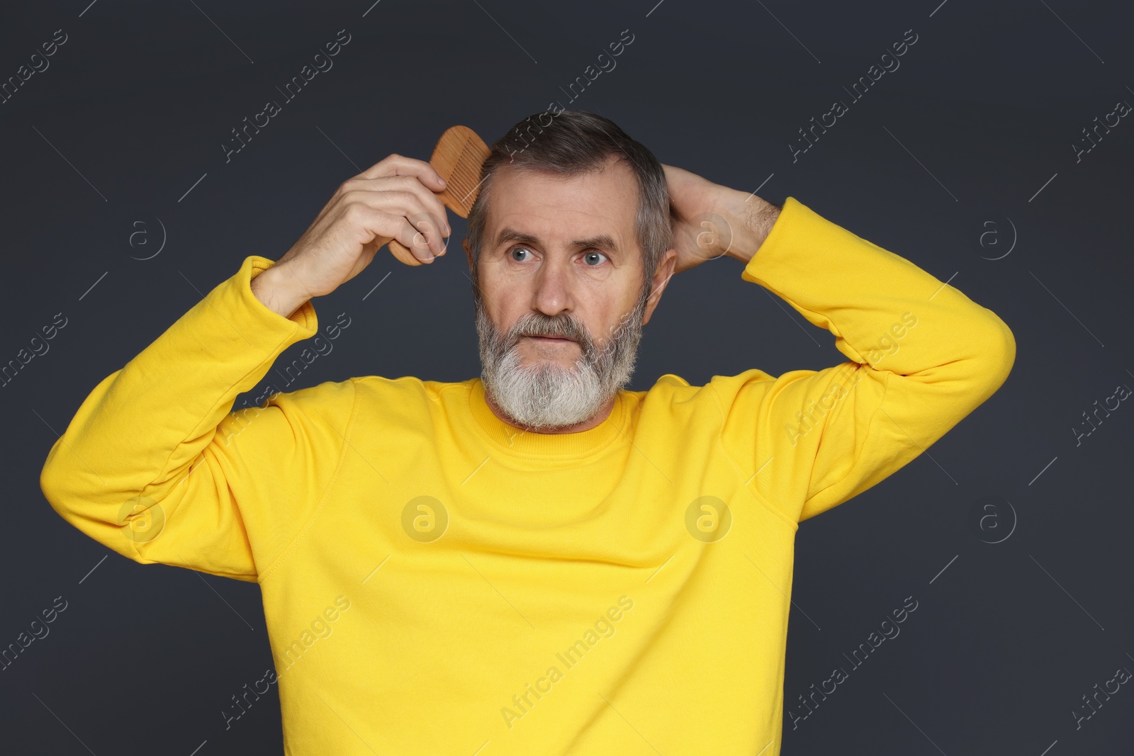 Photo of Handsome man combing his hair on dark grey background