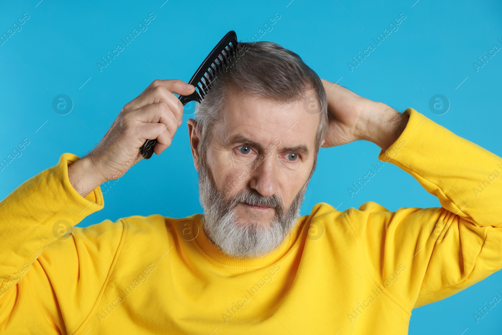 Photo of Handsome man combing his hair on light blue background