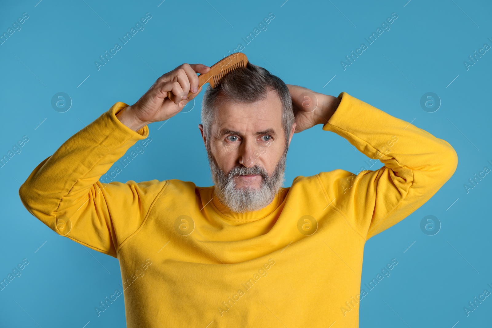 Photo of Handsome man combing his hair on light blue background