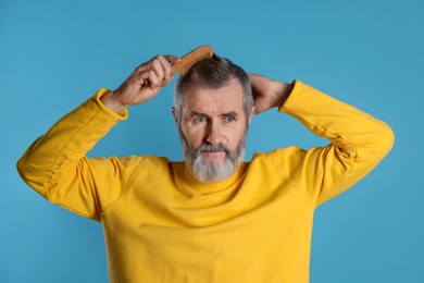 Photo of Handsome man combing his hair on light blue background