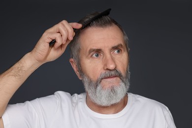 Photo of Handsome man combing his hair on dark grey background