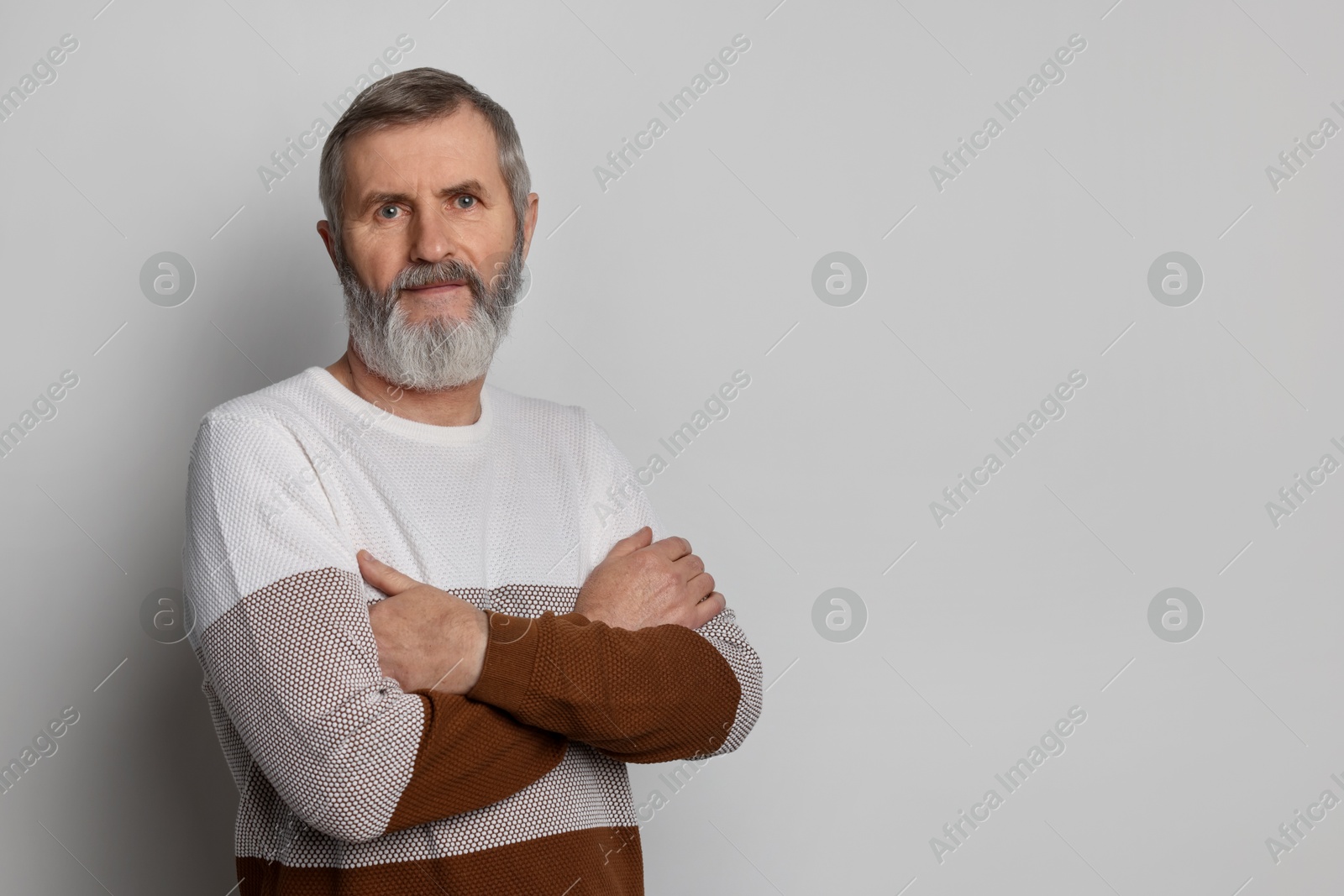 Photo of Portrait of mature man with crossed arms on light grey background, space for text