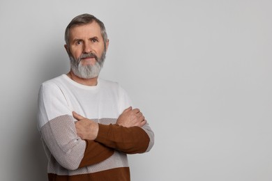 Photo of Portrait of mature man with crossed arms on light grey background, space for text