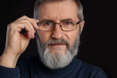 Photo of Portrait of mature man in glasses on black background, closeup