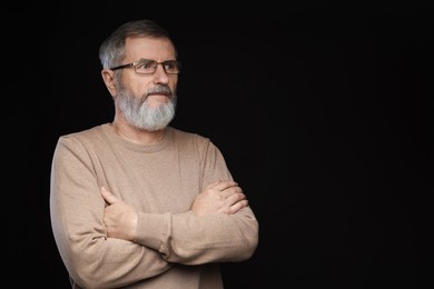 Photo of Portrait of mature man with crossed arms on black background, space for text