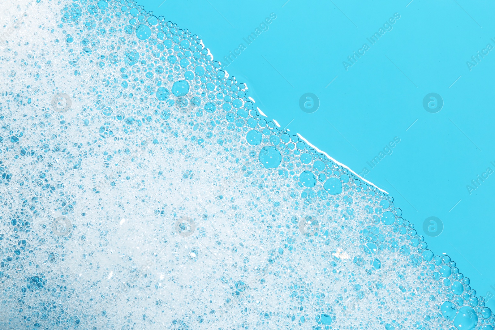 Photo of Detergent foam with bubbles on light blue background, top view