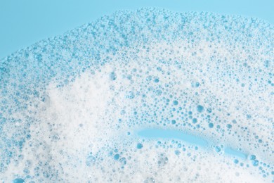 Photo of Detergent foam with bubbles on light blue background, top view