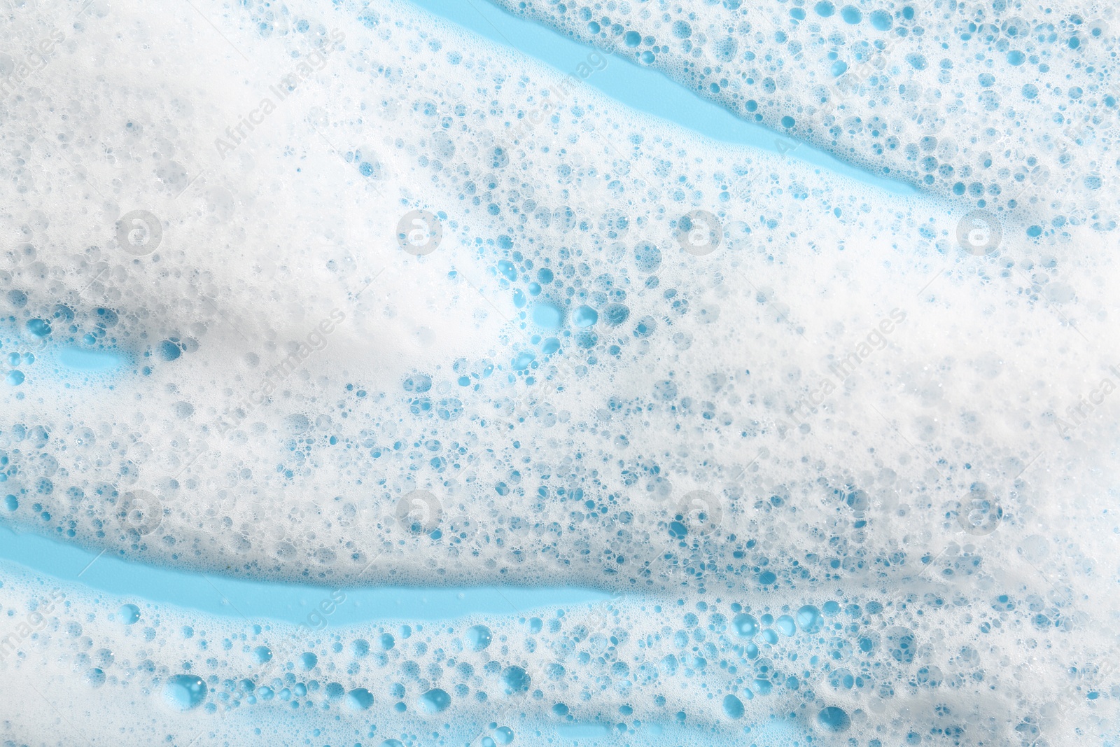 Photo of Detergent foam with bubbles on light blue background, top view