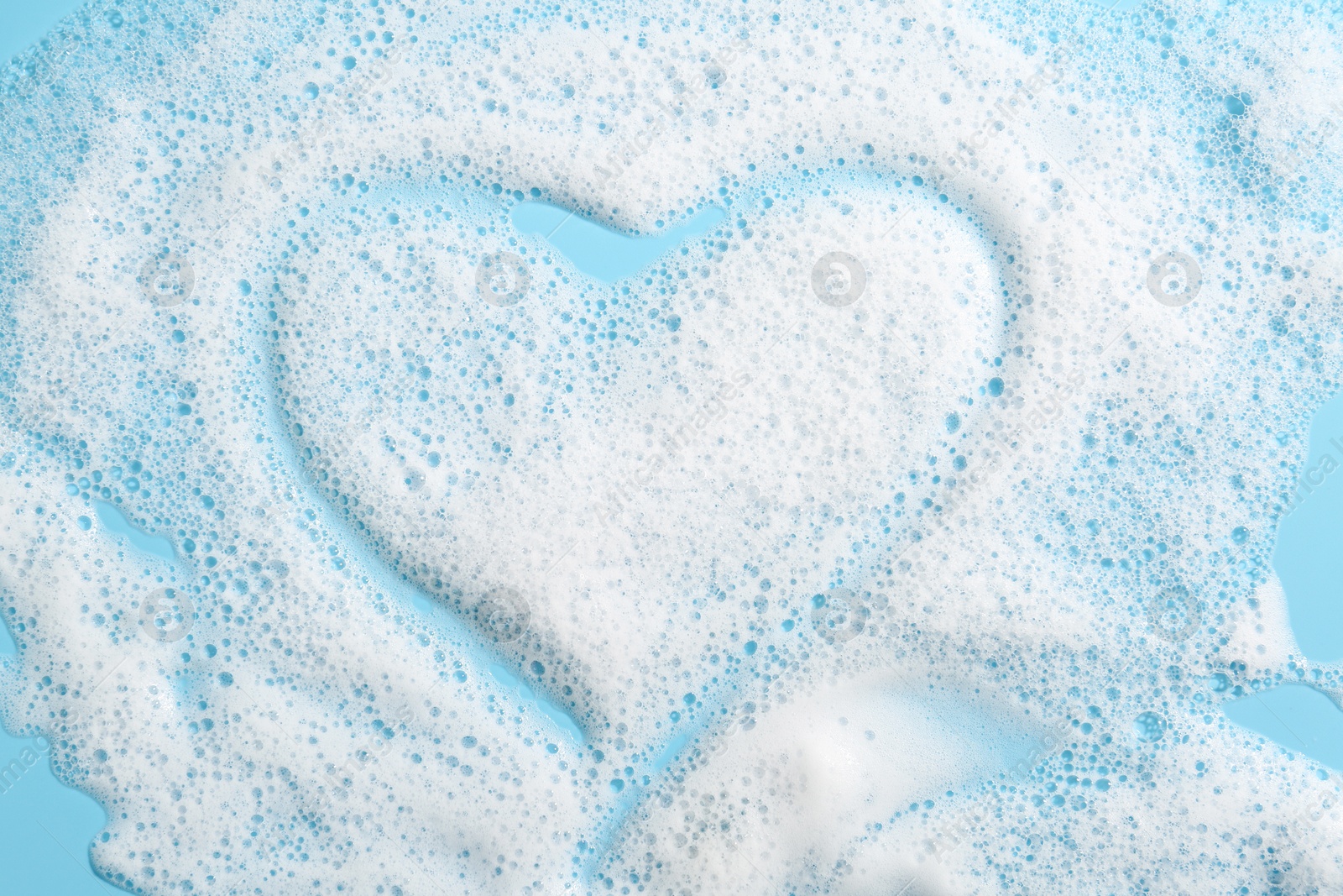 Photo of Heart shape made of detergent foam on light blue background, top view