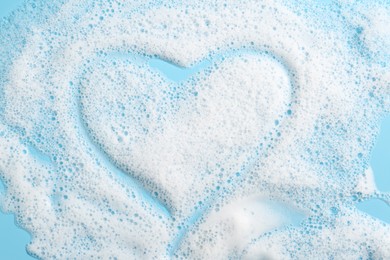 Photo of Heart shape made of detergent foam on light blue background, top view