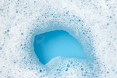 Photo of Detergent foam with bubbles on light blue background, top view