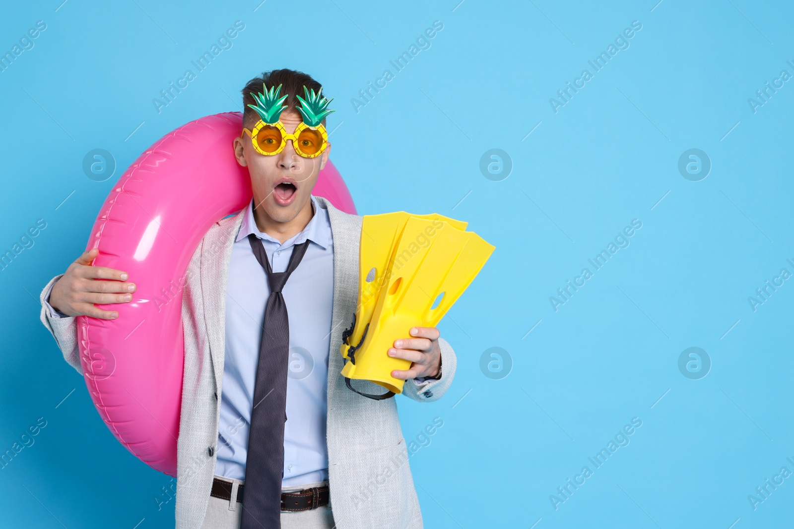 Photo of Businessman with inflatable ring, funny sunglasses and flippers on light blue background, space for text