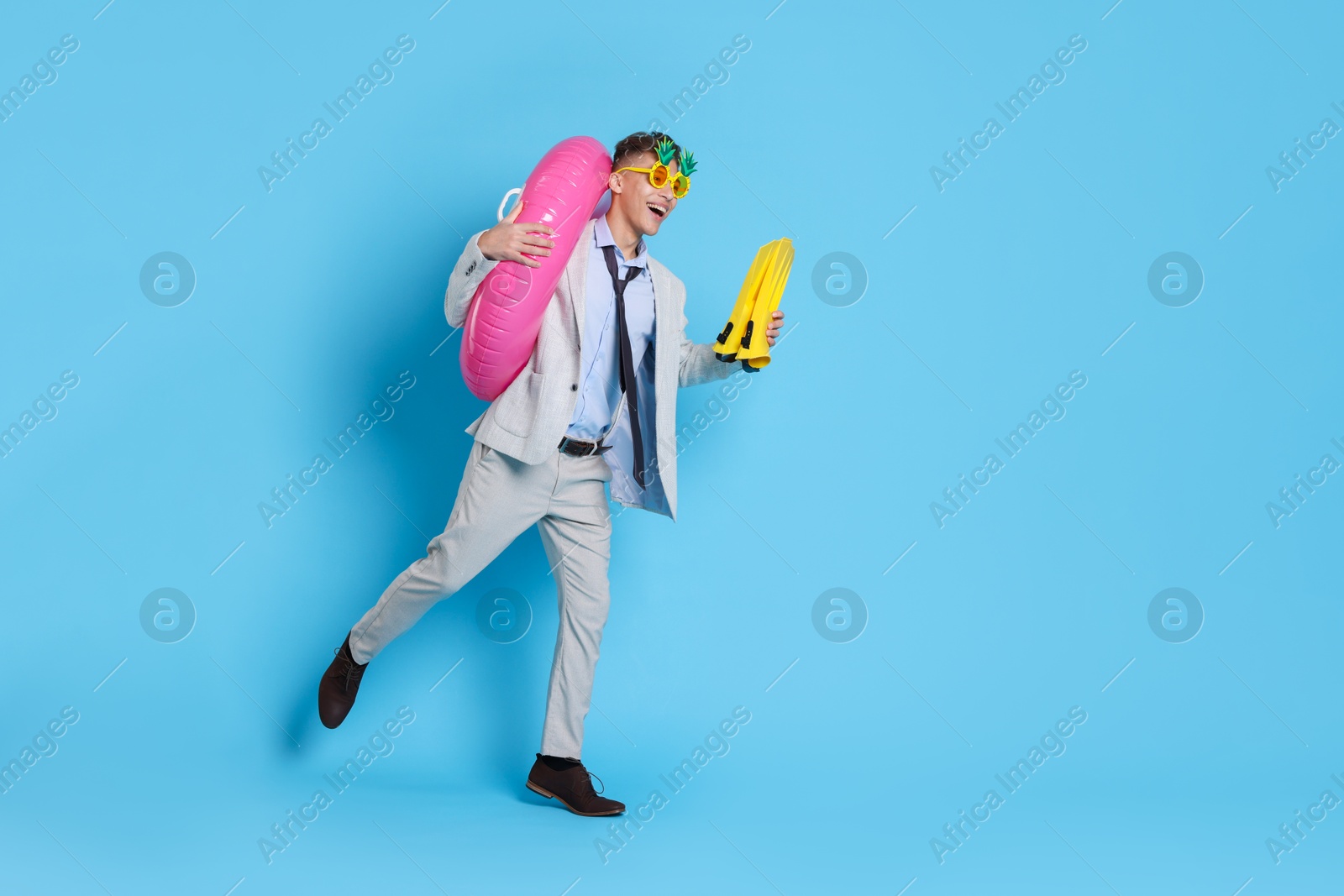 Photo of Businessman with inflatable ring, funny sunglasses and flippers on light blue background, space for text