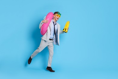 Businessman with inflatable ring, funny sunglasses and flippers on light blue background, space for text