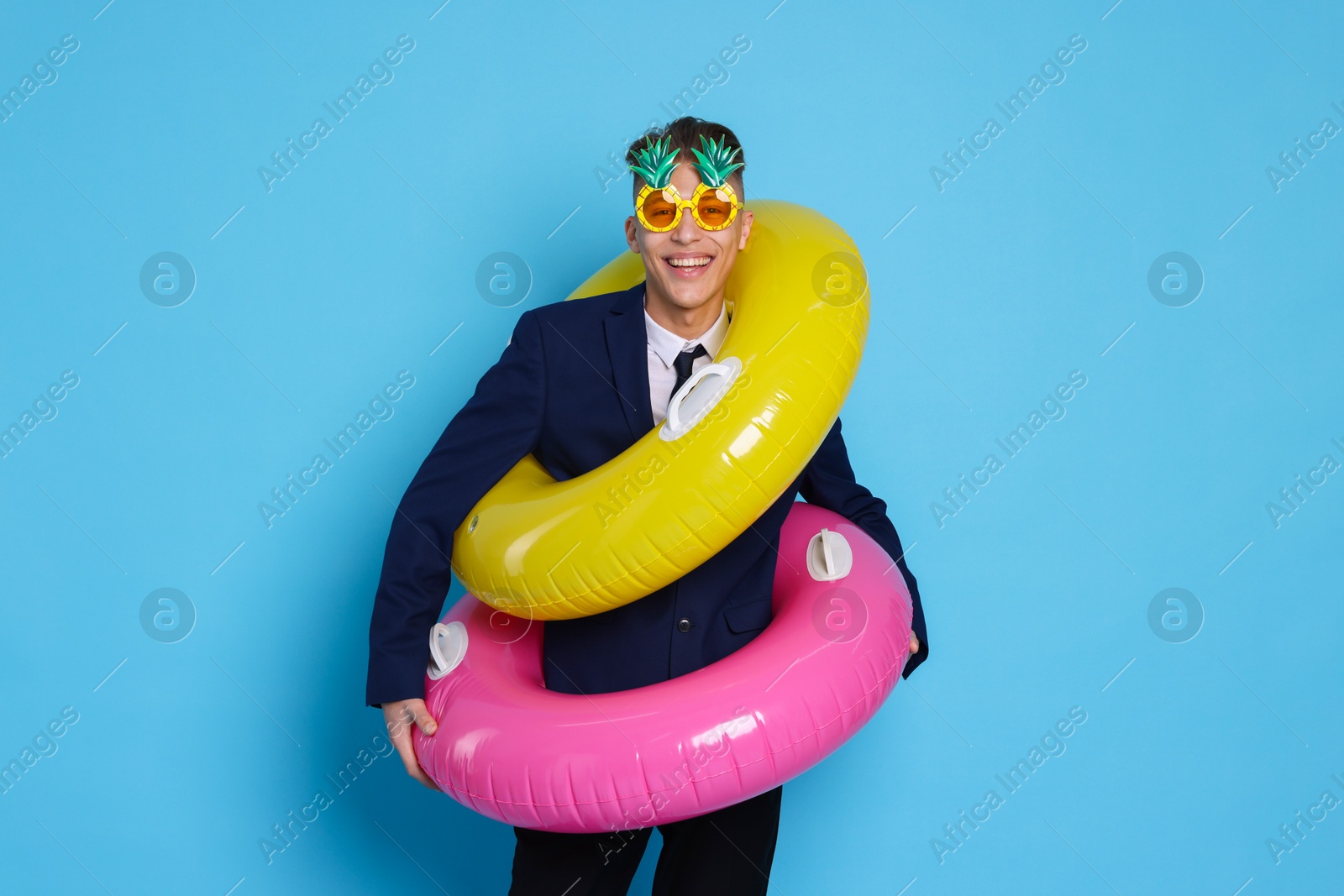 Photo of Businessman with inflatable rings and funny sunglasses on light blue background