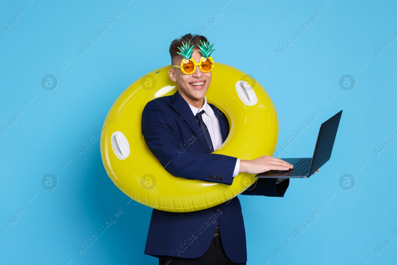 Photo of Businessman with inflatable ring, laptop and funny sunglasses on light blue background