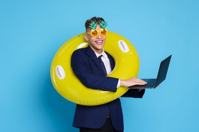 Photo of Businessman with inflatable ring, laptop and funny sunglasses on light blue background