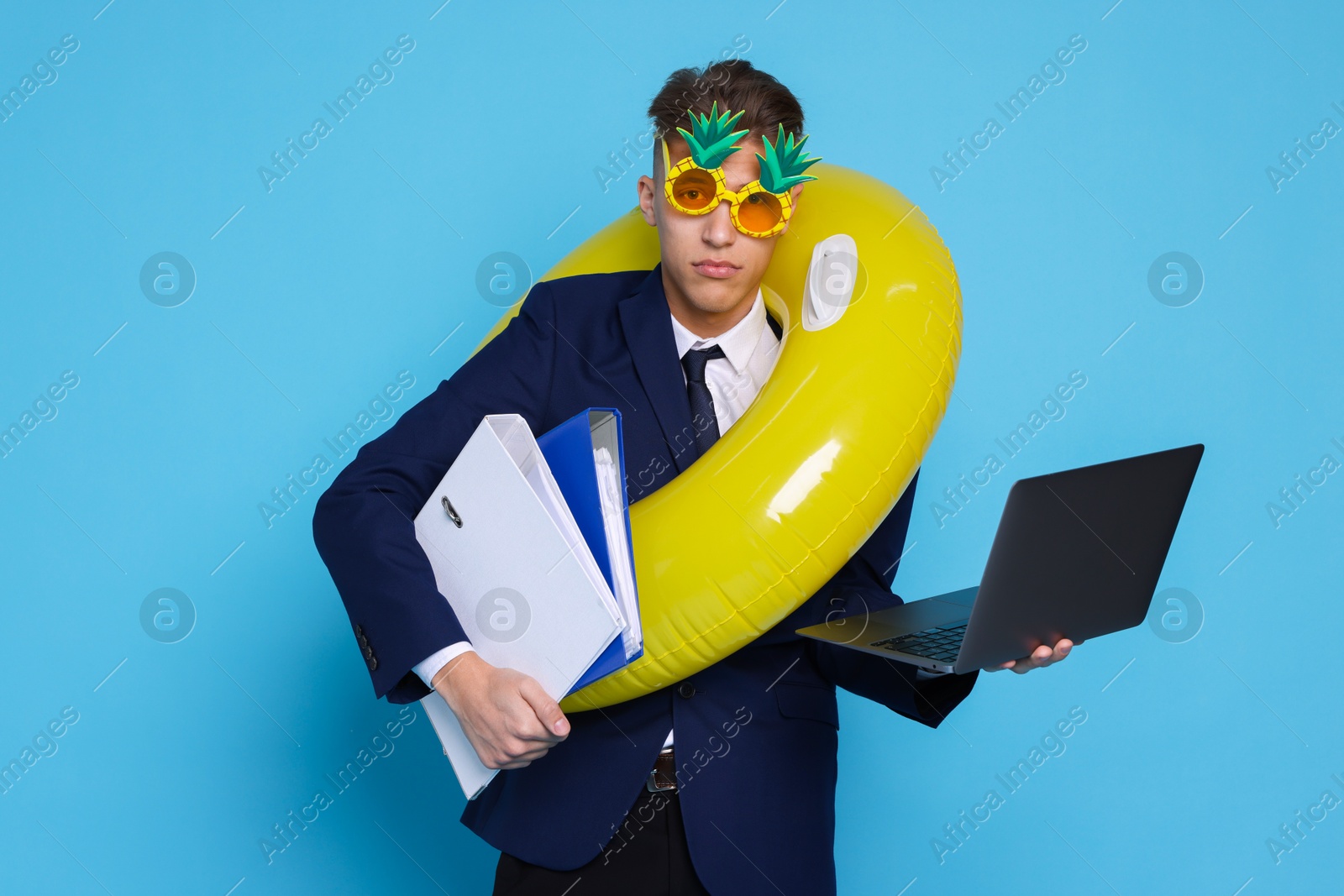 Photo of Businessman with inflatable ring, laptop, folders and funny sunglasses on light blue background