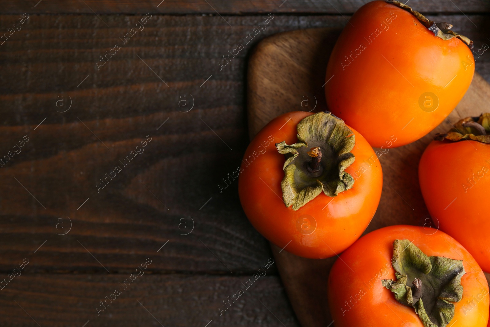 Photo of Delicious ripe juicy persimmons on wooden table, flat lay. Space for text