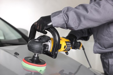 Photo of Man polishing car hood with orbital polisher indoors, closeup