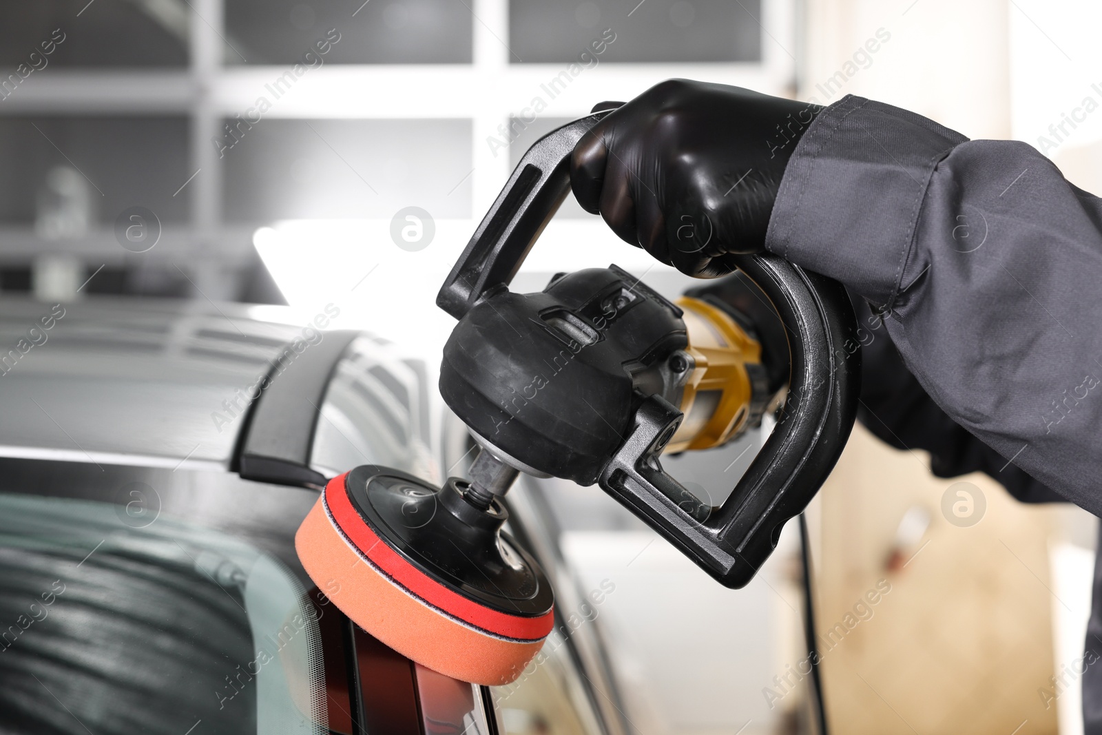 Photo of Man polishing car with orbital polisher indoors, closeup