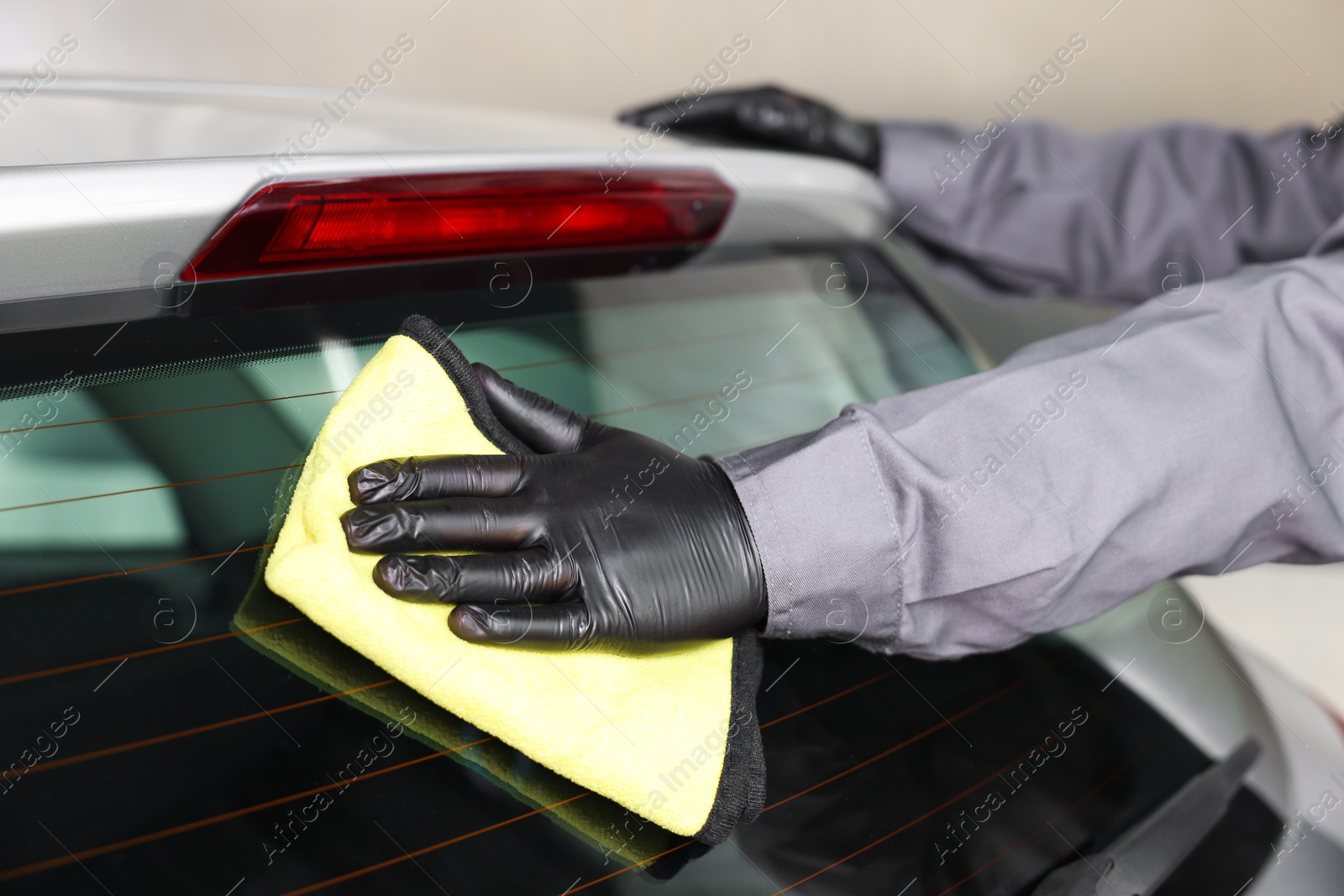 Photo of Man polishing car rear window with yellow rag indoors, closeup