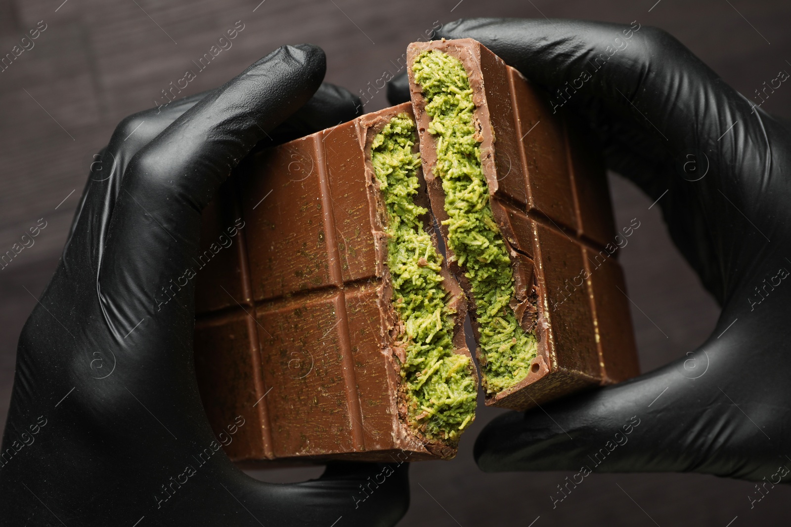 Photo of Woman breaking Dubai chocolate bar with pistachio and knafeh at dark table, closeup