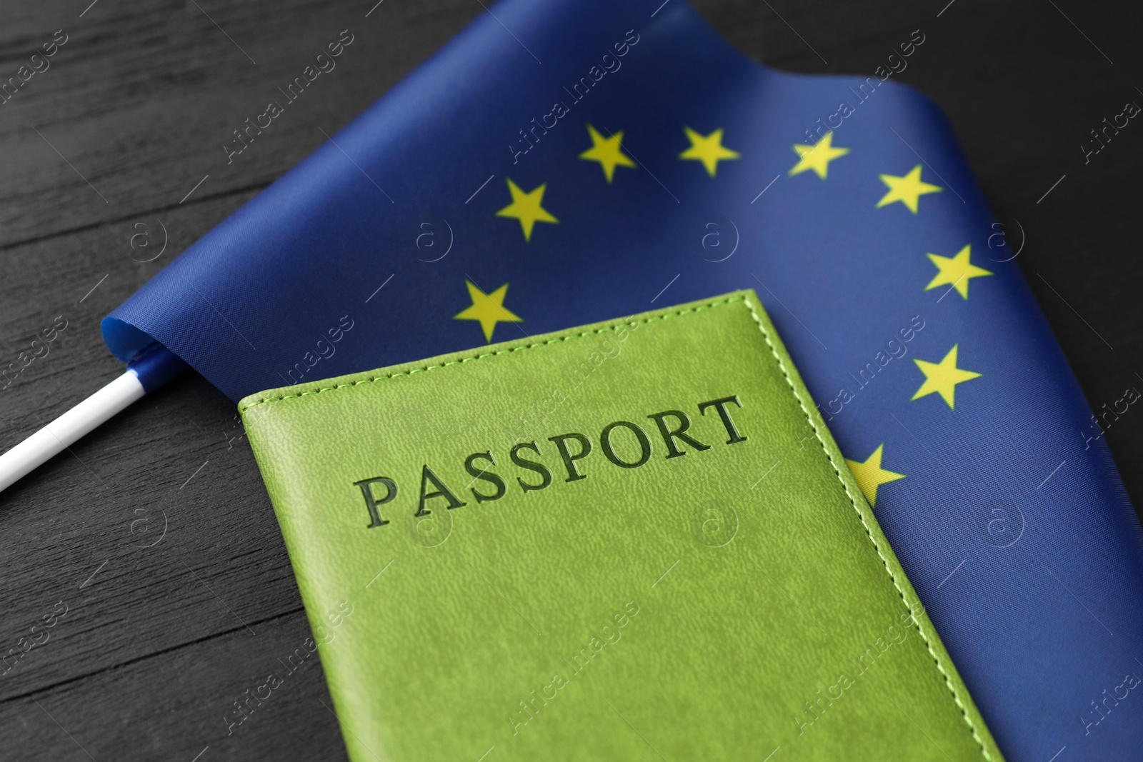 Photo of Passport in green cover and flag of European Union on black wooden table, closeup