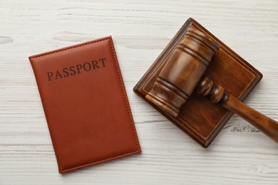 Photo of Passport in brown cover and judge's gavel on light wooden table, top view