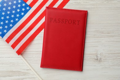 Photo of Passport in red cover and flag of United States on light wooden table, top view