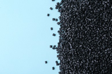 Photo of Pile of black plastic granules on light blue background, top view. Space for text