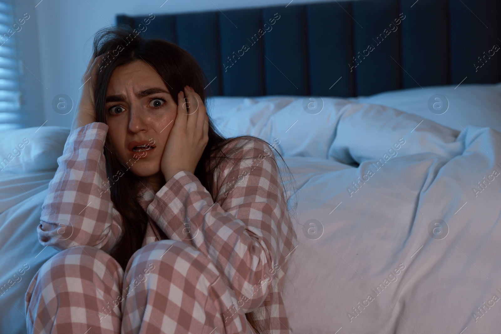 Photo of Fear of darkness. Scared young woman in bedroom at night, space for text