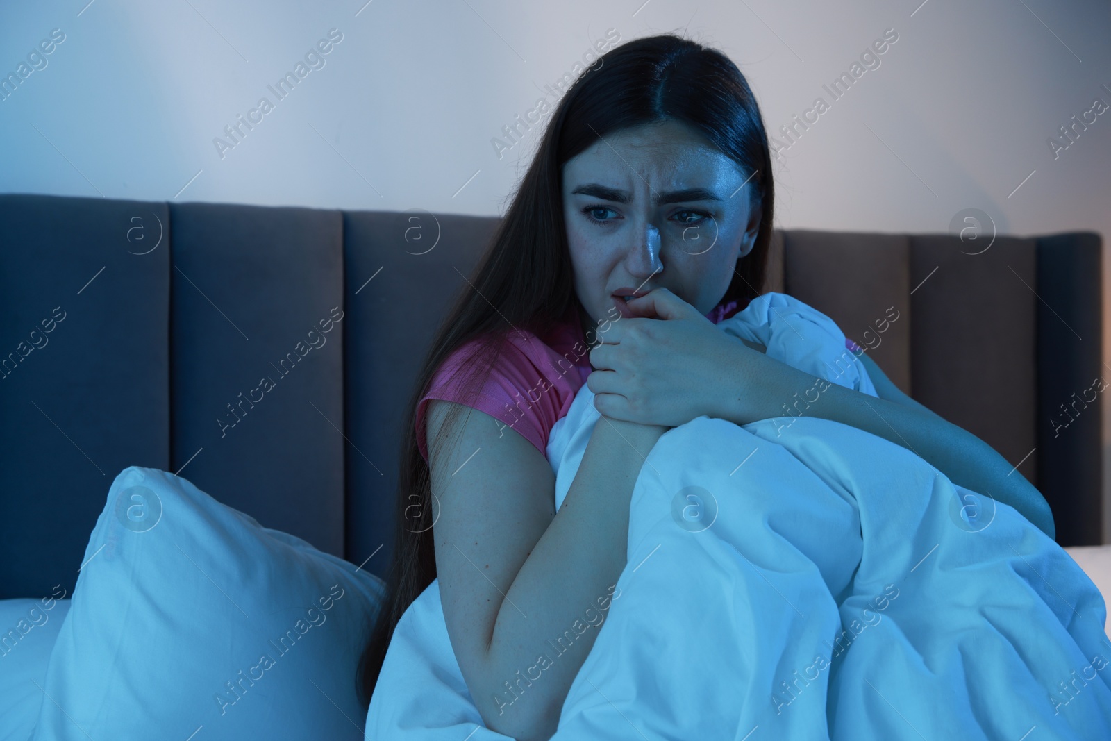 Photo of Fear of darkness. Scared young woman on bed in room at night