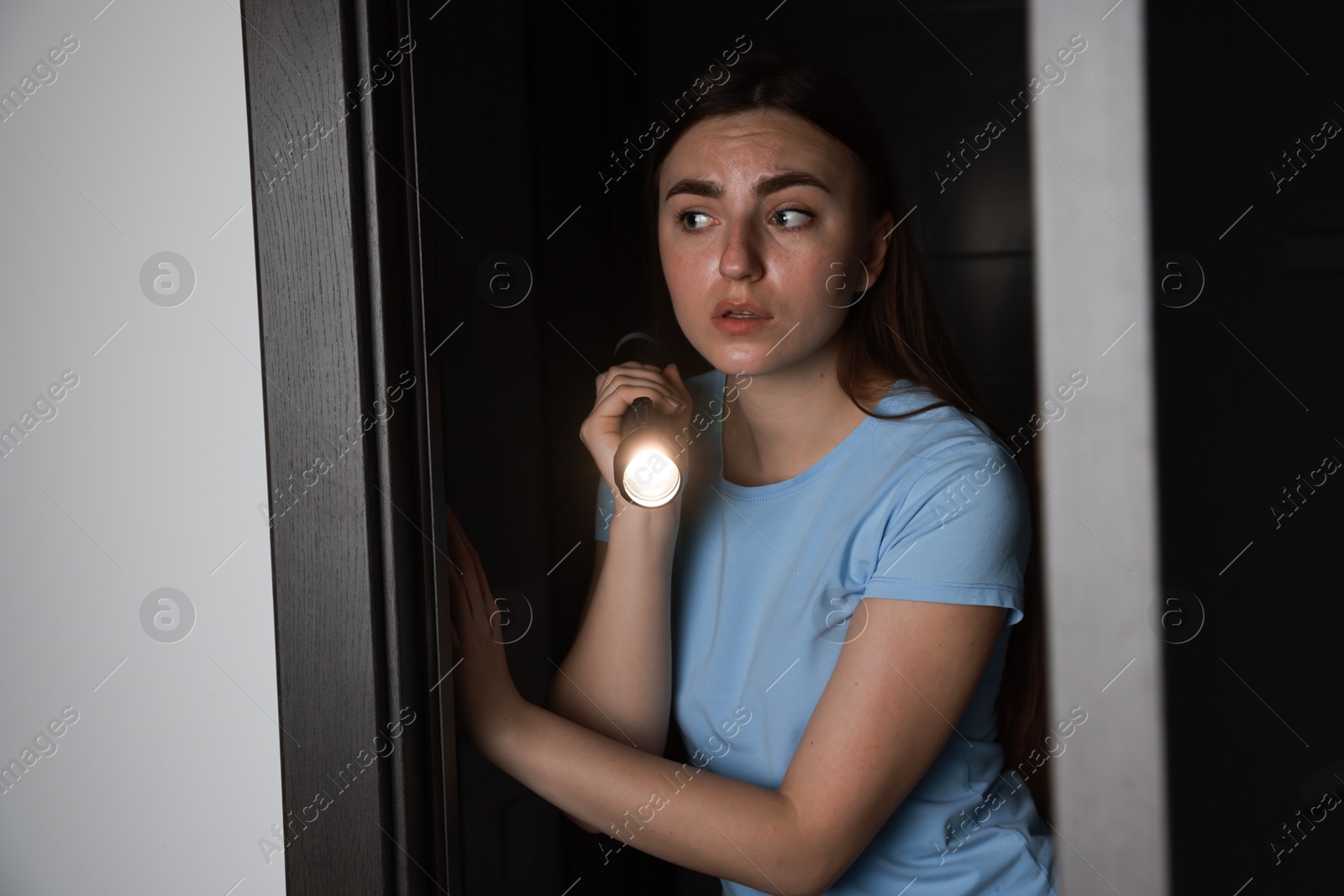 Photo of Fear of darkness. Scared young woman with flashlight indoors at night