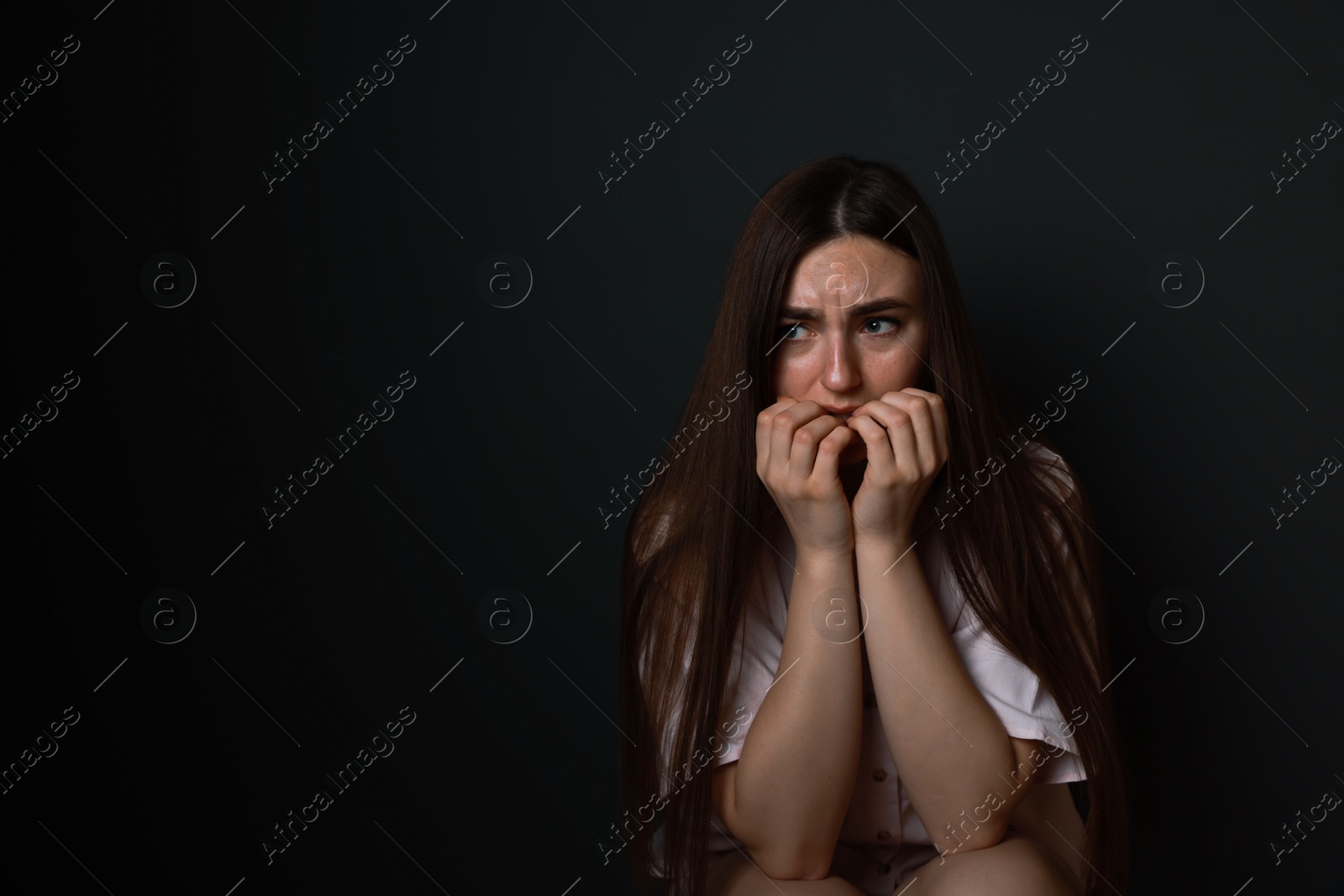 Photo of Fear of darkness. Scared young woman on black background, space for text