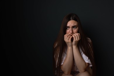 Photo of Fear of darkness. Scared young woman on black background, space for text