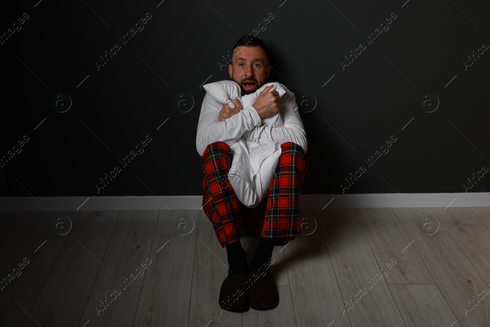 Photo of Fear of darkness. Scared man hugging pillow indoors at night