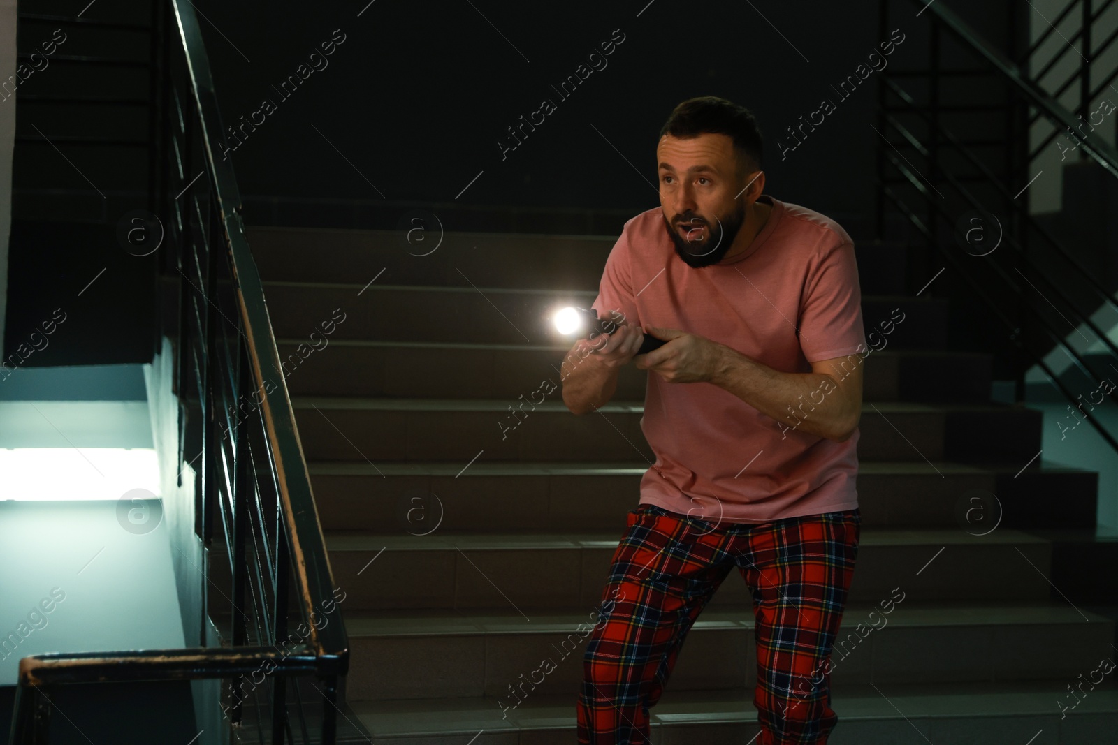 Photo of Fear of darkness. Scared man with flashlight indoors at night, space for text