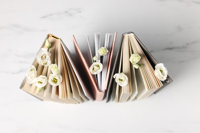 Books and beautiful eustoma flowers on white marble table, top view