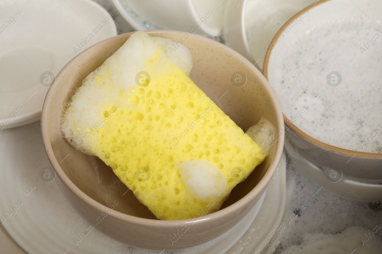 Photo of Yellow sponge, dishes and foam in sink, closeup