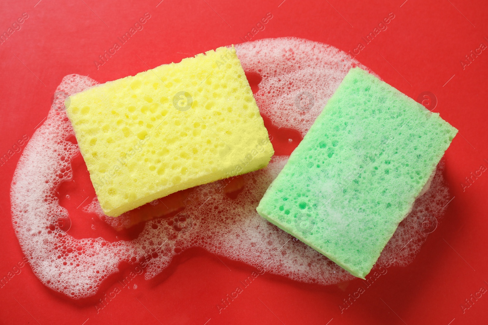 Photo of Two cleaning sponges and foam on red background, top view