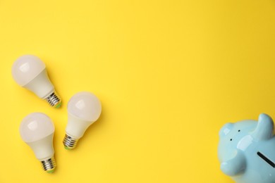 Photo of Piggy bank and light bulbs on yellow background, flat lay with space for text. Energy saving concept