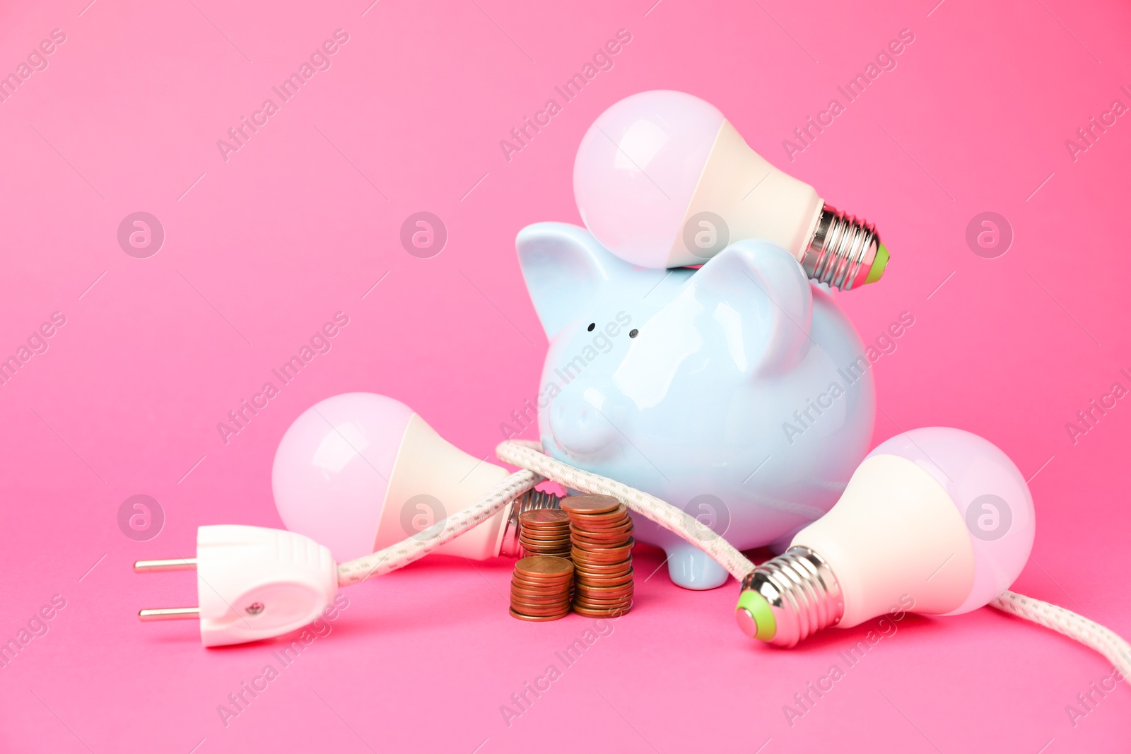 Photo of Piggy bank, light bulbs, coins and plug on pink background. Energy saving concept