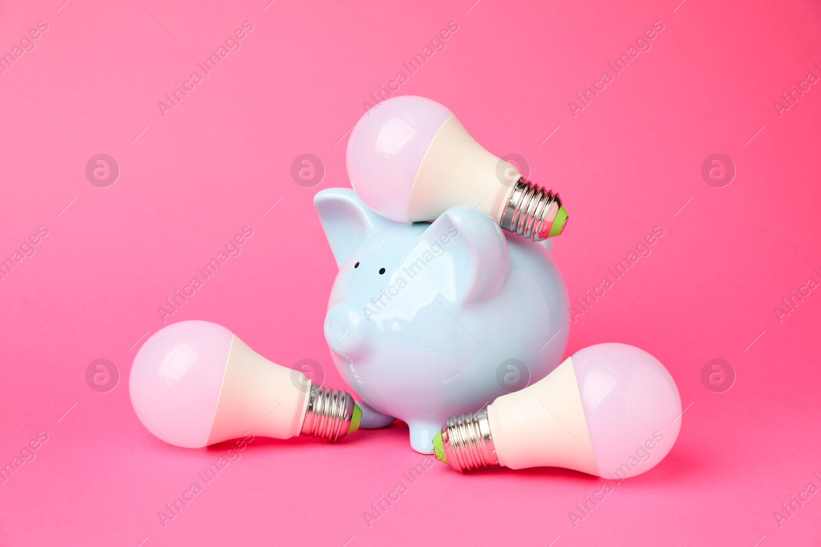 Photo of Piggy bank and light bulbs on pink background. Energy saving concept