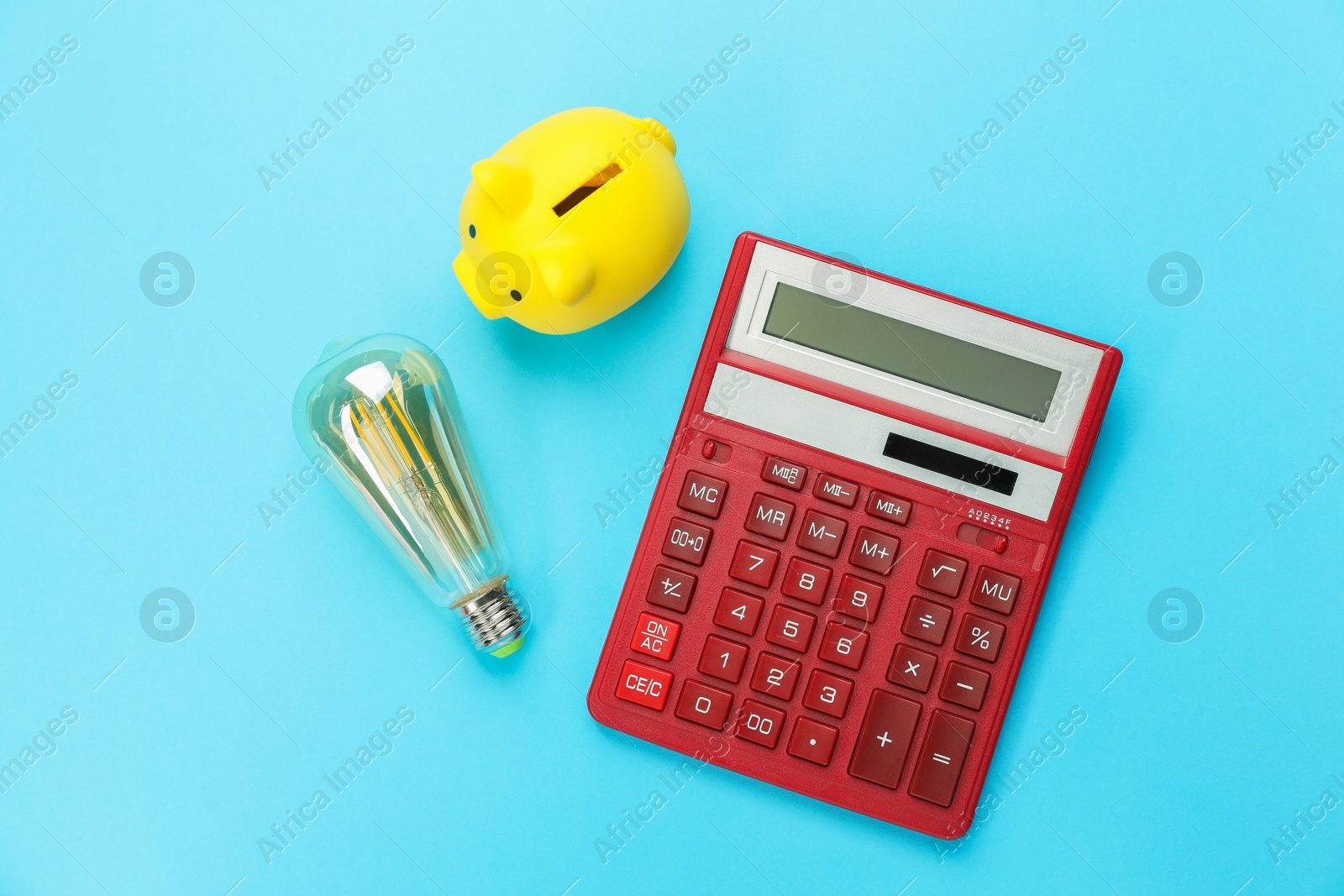 Photo of Piggy bank, calculator and lightbulb on light blue background, flat lay. Energy saving concept