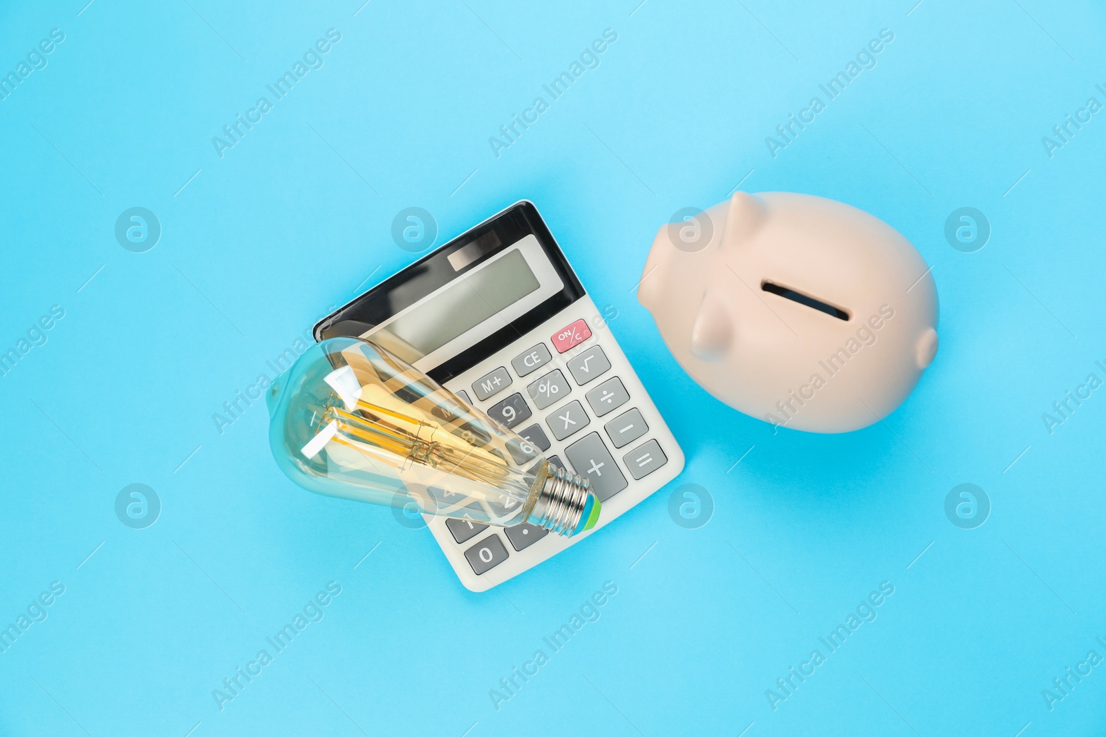 Photo of Piggy bank, calculator and lightbulb on light blue background, flat lay. Energy saving concept