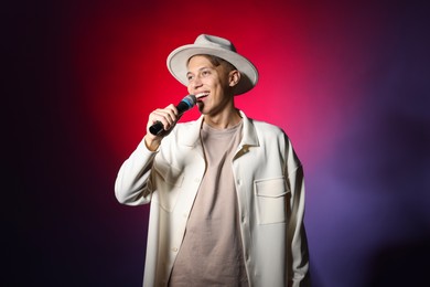 Photo of Talented young man singing on dark background with red light